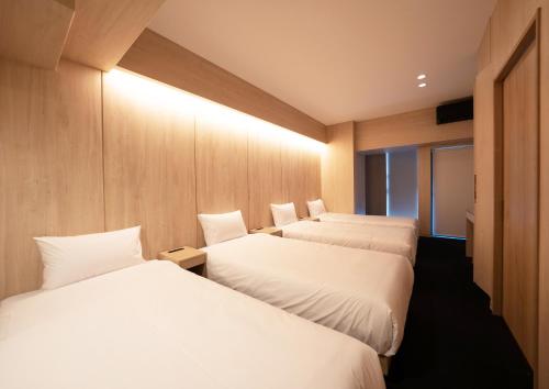 two beds in a hotel room with white sheets at UH Suite Namba Station in Osaka