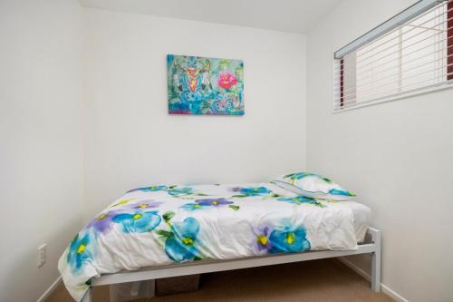 a bed in a white room with a picture on the wall at 5 Minute Stroll To The Beach in Orewa