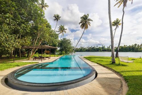 a swimming pool next to a lake with palm trees at Cranganor History Café & Riverside Château in Parūr