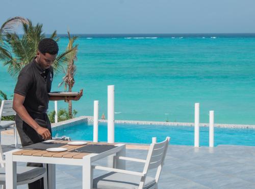 a man standing next to a table next to the ocean at Oasis Blu Beach Resort-Adults Only in Nungwi