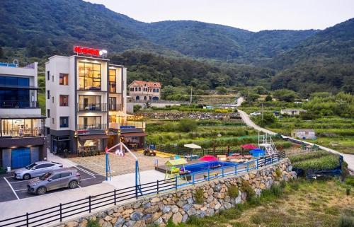 a building with a parking lot next to a mountain at Geoje Harakeke Pension in Geoje 