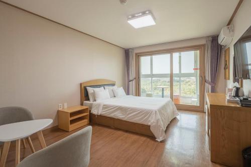 a bedroom with a bed and a table and a window at Jeju Amor House Oceanview Oreum in Jeju
