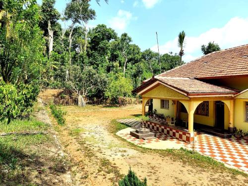a yellow house with a porch next to a field at Malnad Bliss in Sringeri