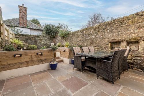 a patio with a table and chairs and a stone wall at Logies Cottage in St. Andrews