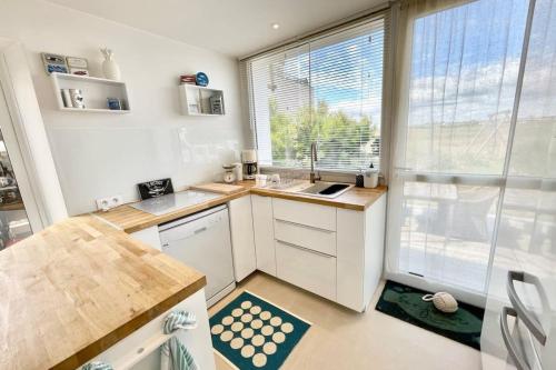 une cuisine avec des placards blancs et une grande fenêtre dans l'établissement Maison Ultra Coconning Jardin Face aux plages, à Ploemeur