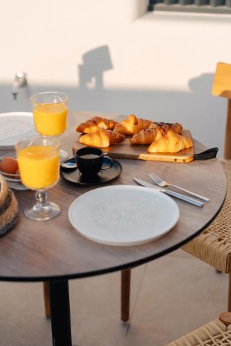 a table with a plate of bread and glasses of orange juice at Erthā Suites with private pools in Vóthon