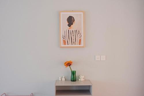 a white wall with a picture and a vase with flowers on a table at Ponder Bali Canggu in Canggu