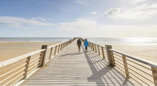 2 personnes marchant sur une promenade en bois jusqu'à la plage dans l'établissement Appartement face mer, à Saint-Jean-de-Monts