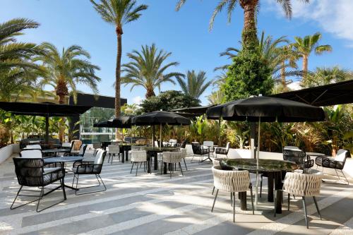 a patio with tables and chairs and palm trees at Ushuaïa Ibiza Beach Hotel - Adults Only - Club Entrance Included in Playa d'en Bossa
