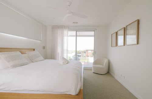 a white bedroom with a bed and a chair at Oceanview Escape - Luxe Coastal Retreat with Hot Tub in Surf Beach