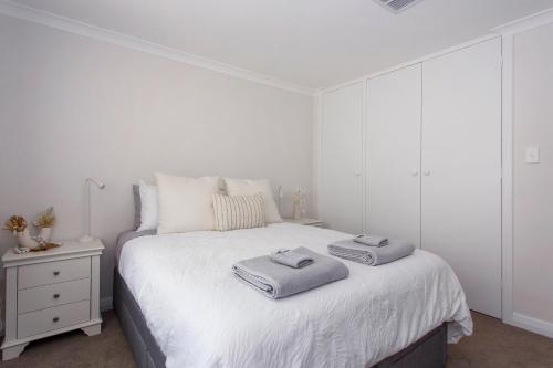 a white bedroom with a bed with two towels on it at Maylands Riverside City Retreat in Perth