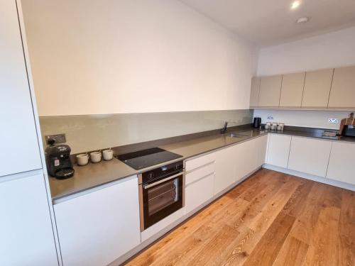 a kitchen with white cabinets and a wooden floor at Luxury Altrincham Apartment by City SuperHost in Altrincham