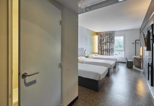 a hotel room with three beds and a sliding door at B&B HOTEL Ouistreham in Ouistreham