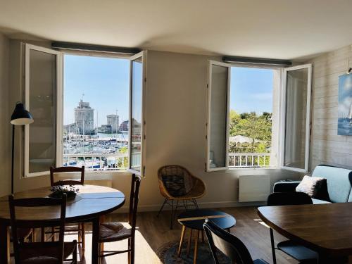 un salon avec une table, des chaises et des fenêtres dans l'établissement Appartement vue port - quai valin, à La Rochelle