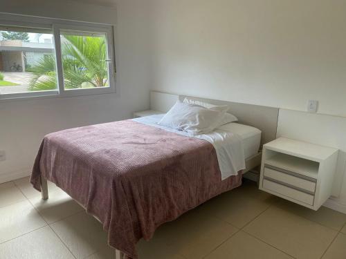 a white bedroom with a bed with a window at Casa Condomínio Ocean Side Alto Padrão - Pé na Areia in Torres