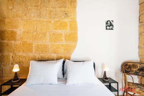 a bed with white pillows and a brick wall at Charming Village Escape with Jacuzzi & Games Room in Rabat