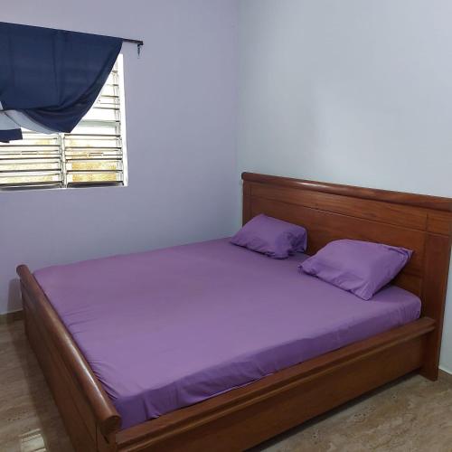a bed with purple sheets in a room with a window at Le séjour fruité in Ouidah