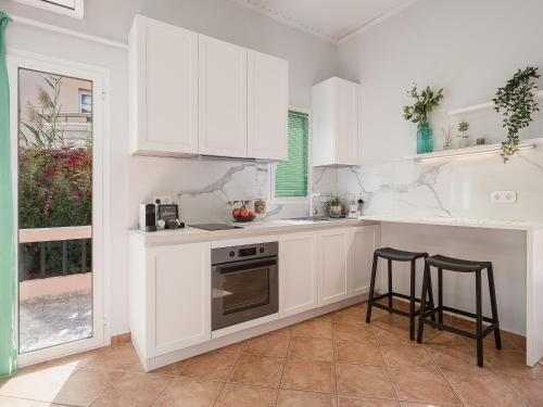 a kitchen with white cabinets and a stove and stools at Elena Seafront Luxury Apartments in Almirida