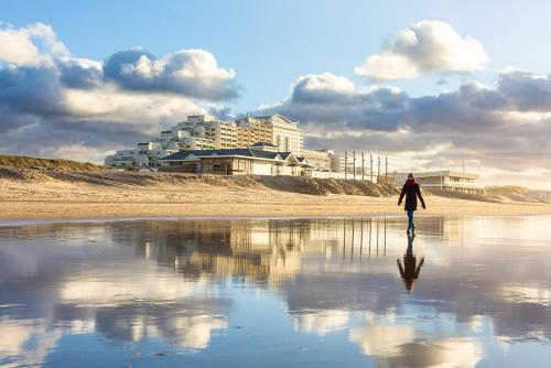 a person walking on the beach with a building in the background at Hello Noordwijk - Familiehuis Quarles van Uffordstraat 77 in Noordwijk aan Zee