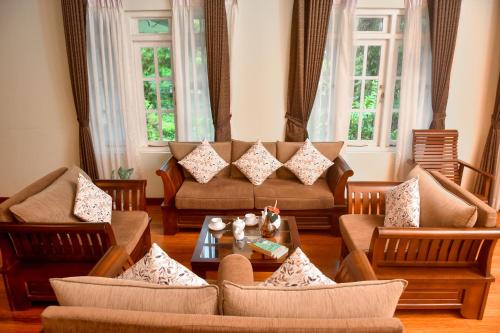 a living room with couches and tables and windows at Tea Queens Bungalow in Hatton