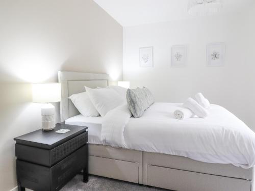 a white bedroom with a white bed and a night stand at Aelfor in Harlech