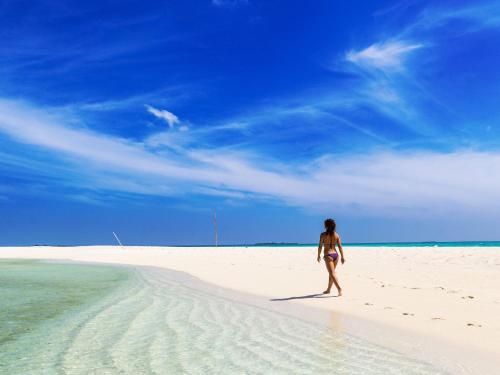 a woman walking on a beach in the sand at Feridhoo Inn in Feridhoo