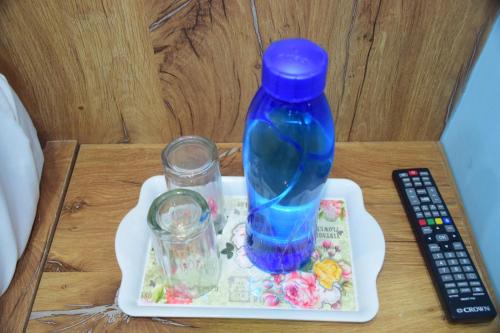 a blue bottle on a tray with two glasses and a remote control at JMB Hotel Rana Palace in Dewās