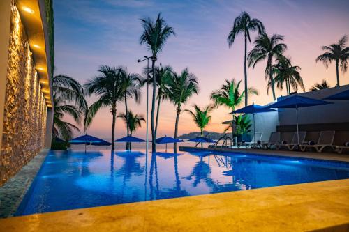 アカプルコにあるRitz Acapulco All Inclusiveのヤシの木と傘が備わる大型スイミングプール