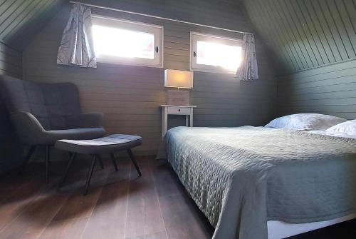 a bedroom with a bed and a chair and two windows at Vier Winde Usedom - Ferienanlage in Krummin