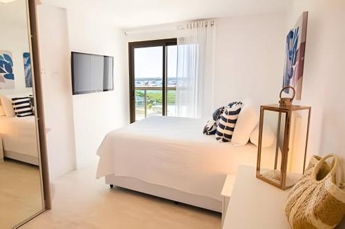 a white bedroom with a bed and a window at Arraial | Apartamento com 3 suítes e Vista Mar in Arraial do Cabo