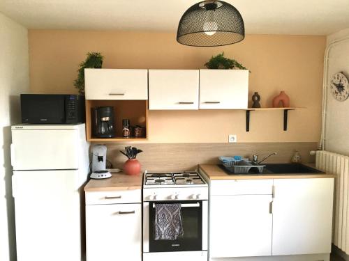 une cuisine avec des armoires blanches et un four à plaques de cuisson dans l'établissement Fleur de lumiere, au Creusot