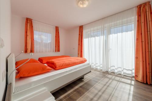 a bed with orange pillows in a room with windows at Garni B&B Apartments Plank in Nova Levante