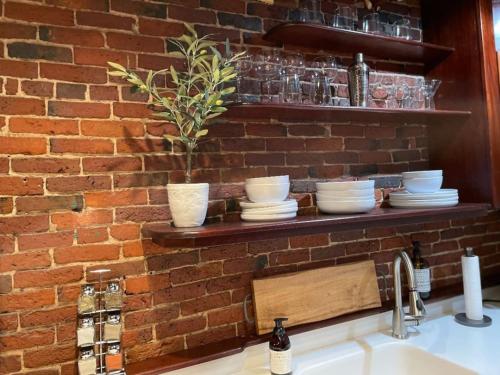 a brick wall with dishes on a shelf above a sink at City Loft Group Getaway King Downtown Location in Newburyport