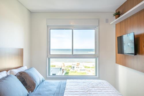 a bedroom with a bed and a large window at Aptos Pé na Areia Vista Mar Condomínio Resort Completo com Piscina borda Infinita, Beach Tennis, Academia, Sala de Jogos, Brinquedoteca, Playground e Portaria 24H 3 Quartos com Ar-Condicionado, Churrasqueira Privativa Reserve Agora e Viva essa Experiência in Piçarras