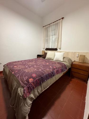 a bedroom with a bed with a purple blanket and a window at La Escondida de la Aldea Serrana in Valle Hermoso