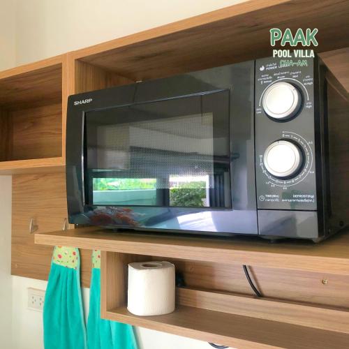 a black microwave oven sitting on a wooden shelf at PAAK Pool Villa Cha-am in Cha Am