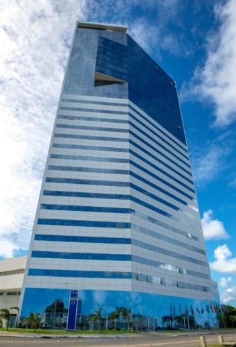 a tall glass building with a blue sky at Ezza Experience - Beach Flat in Recife