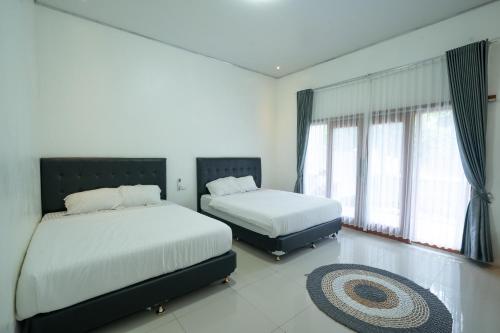 two beds in a room with two windows and a rug at Kinkeo Borobudur in Magelang