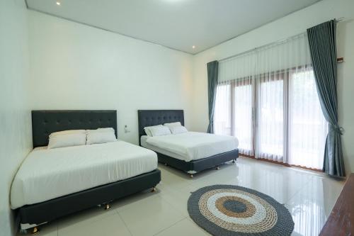 two beds in a room with two windows and a rug at Kinkeo Borobudur in Magelang