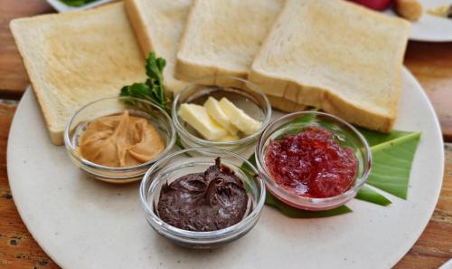 a plate of food with bread and jam and dips at Sadi Beach House in Telukbakau