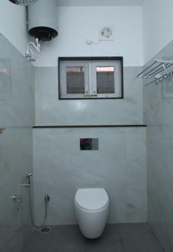 a white bathroom with a toilet and a window at Kaveri Homestay in Suntikoppa