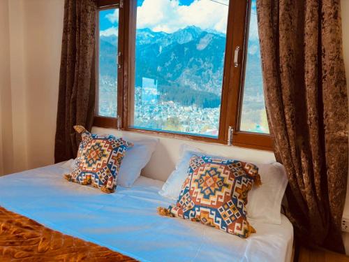 a bed with pillows in front of a large window at hotel in manali by Aura in Vashisht