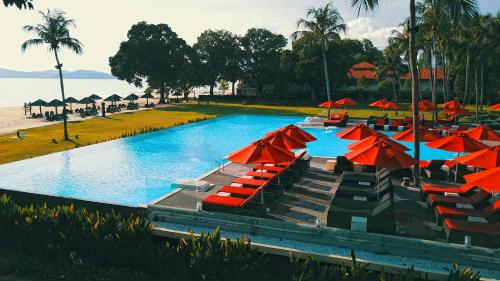 a large swimming pool with red umbrellas and chairs at Holiday Villa Resort & Beachclub Langkawi in Pantai Cenang