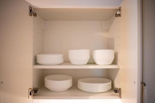a cupboard filled with white plates and bowls at Platz für 8 Pers - C4S Come4Stay Monteure "InnArt" Boxspringbett Einzelbett Töging am Inn, Parkplatz, WLAN, Balkon, Smart TV, voll ausgestatteter Küche, Waschmaschine in Töging am Inn