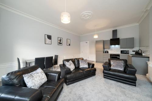 a living room with black leather furniture and a kitchen at Lochside Apartments, Apt C in Montrose