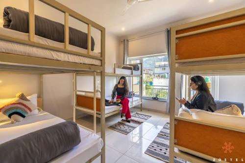 two women sitting in a room with bunk beds at Zostel Rishikesh, Tapovan in Rishīkesh