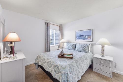 a white bedroom with a bed and two lamps at Relaxing inland condo with pool and steps to beach in Marco Island