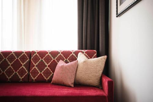 a red couch with two pillows sitting in front of a window at Hotel Cavallino D'Oro Bed&Breakfast in Castelrotto