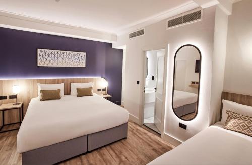 a bedroom with two beds and a mirror at Thistle London Bloomsbury Park in London