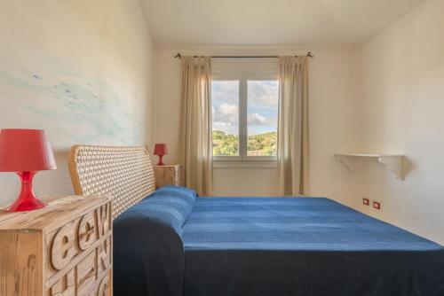 a bedroom with a blue bed and a window at Baia Bianca Apartments Sardinia in Baja Sardinia